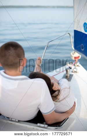 Back view of beautiful young loving couple sitting and hugging on yacht with sail