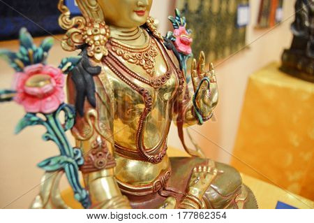 Golden statue of a buddha with a smile. Flowers in hands