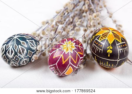 Hand painted eggs with ethnic pattern and ancient symbols with willow twigs on white fabric tablecloth. Light Easter background. Ukrainian pysanka. Close shot.