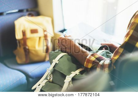 Enjoying travel. Young hipster smile man with backpack traveling by train sitting near the window holding in hand and looking map. Tourist in summer shirt planing route of railway railroad transport concept