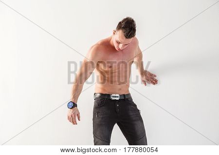 Sexy muscular man body posing at white wall, black jeans