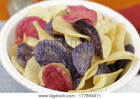 Red yellow and purple potato chips in a bowl close-up. Red white and blue theme food potato chips made from Crimson Purple Majesty and Chipeta or Atlantic potatoes