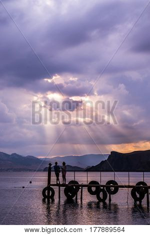 Silhouettes of men and women standing on the pier in the background of mountains and sea stress-rays of the setting sun. Romantic atmosphere and natural beauty of a meditation relaxation meditation expression of feelings.