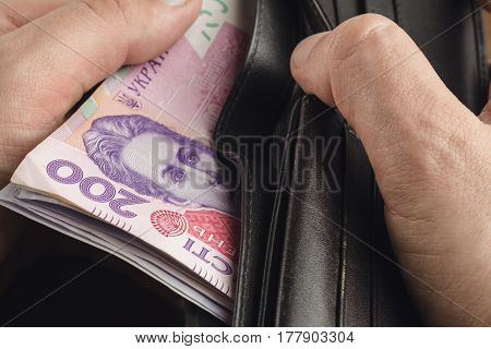 Close-up view of male hands opened the wallet with ukrainian money currency hryvnia on wooden background