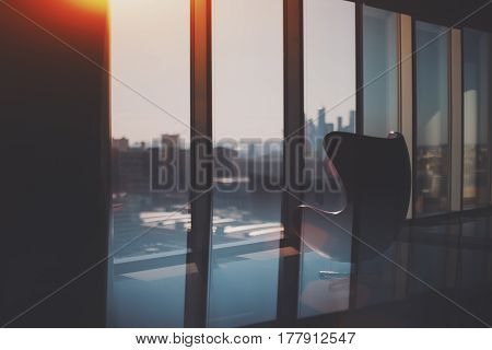 Silhouette of empty curved armchair standing on reflective floor of modern office next to window with cityscape outside and silhouettes of Moscow City business skyscrapers group on sunny day