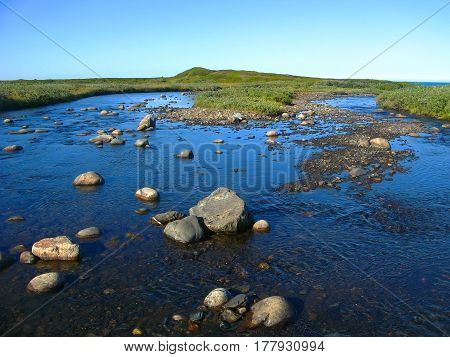 Background blurred view landscape shallow river flowing over the plateau and flowing into the Barents Sea on the Rybachiy peninsula, Murmansk region