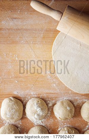 The prepared dough with flour and with a rolling pin. On a wooden table.
