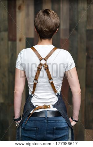 Young woman chef or waiter posing, wearing apron and t-shirt on wooden background