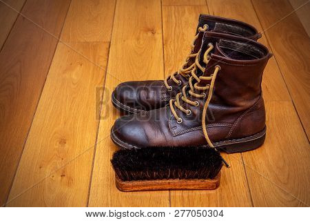 Brown Leather Boots And A Shoe Brush On A Wooden Floor