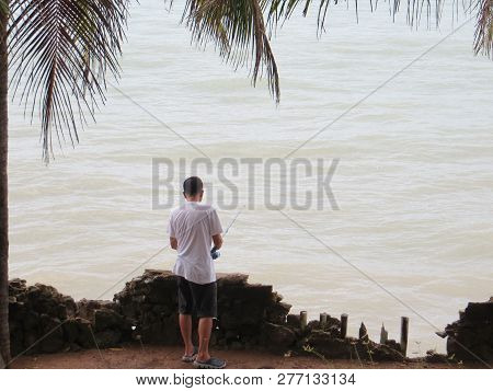Anyer, Indonesia - June 25, 2018: A Man Standing On The Edge Of The Cliff Fishing In The Sea.