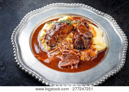 Traditional German braised veal cheeks in brown sauce with mashed potatoes as closeup on a pewter plate 