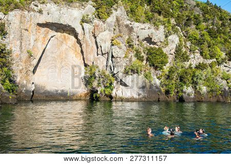 Taupo, New Zealand - April 24 2017: Tourist Swimming In Great Lake Taupo In Front Of Maori Rock Carv