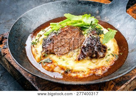 Traditional German braised veal cheeks in brown sauce with mashed potatoes and beans as closeup in a wrought-iron pan