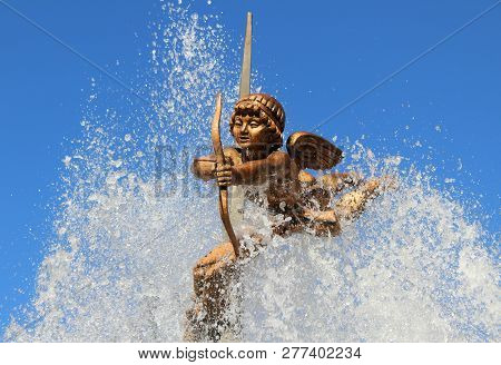 The Figure Of Cupid With A Bow And Arrows On Which Water Flows From The Fountain