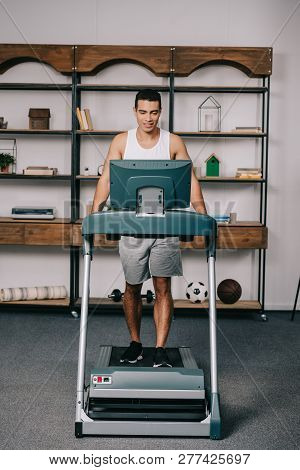 Cheerful Muscular Bi-racial Man Exercising On Treadmill In Living Room