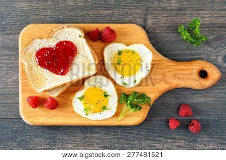 Valentines Day Brunch Concept With Heart Shaped Eggs And Toast With Jam On A Paddle Board. Top View 