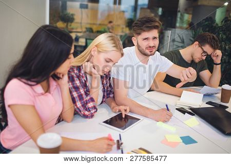 Unhappy And Upset Young Man Hold Big Thumb Down. He Is Dissapointed. Another People In Team Works. T