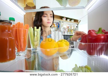 Portrait Of Female Standing Near Open Fridge Full Of Healthy Food, Vegetables And Fruits. Portrait O