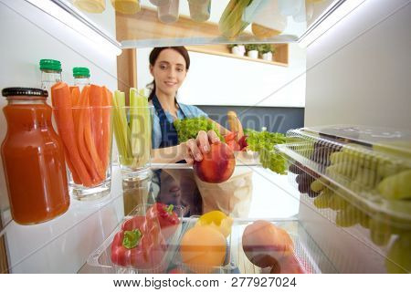 Portrait Of Female Standing Near Open Fridge Full Of Healthy Food, Vegetables And Fruits. Portrait O
