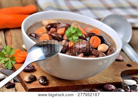 Close-up Of Bean Soup With Large Beans , Spoon, Carrots, Parsley And Marjoram, Towel And Ladle In Ba