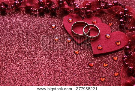 Red Background With Two Rings And A Heart, Near Small Glass Hearts And Beads With A Ribbon