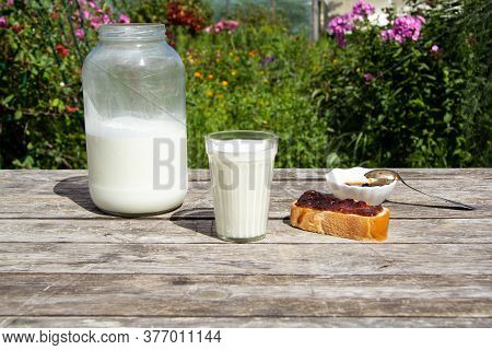 A Faceted Glass Of Milk Stands On A Wooden Table. There Is A Large Two-litre Can Of Milk Nearby. On 