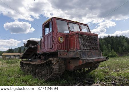 An Old Logging Truck, Rusty And Abandoned In A Field Against The Backdrop Of A Beautiful Forest, As 