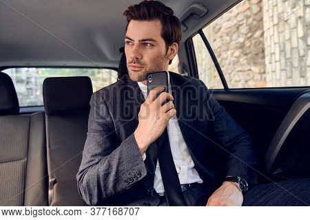 Portrait Of Confident Young Business Man In Full Suit Looking Away Seriosly With Mobile Phone In Han
