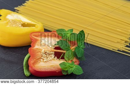 Raw pasta on the table with vegetables, papryka, radish and mint.