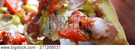 Close-up Of Persons Hand Taking Delicious Slice Of Baked Pizza. Bacon Sausages Double Cheese And Tom