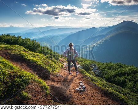 Beautiful Mountains And Standing Young Woman With Backpack On The Trail At Sunset In Summer. Landsca
