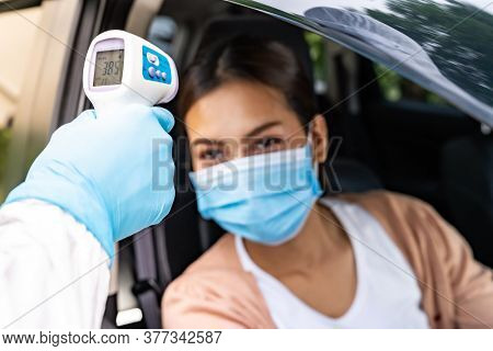 Medical staff with PPE Take Temperature for fever to asian woman before coronavirus covid-19 test at drive thru station in hospital. New normal healthcare drive thru service and medical concept.
