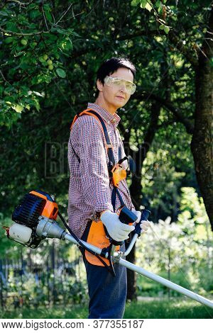 Portrait Of Woman Gardener Mowing The Grass On Backyard Using String Trimmer