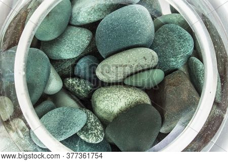 Sea Stones Turquoise In Water In A Glass Vase From Above On A White Background