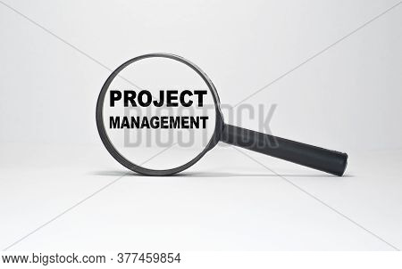 Magnifying Glass With Text Project Management On Wooden Table.