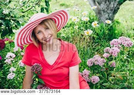 Cottagecore And Staycation At Home. Happy Elderly Blonde Woman In Hat Resting Among Flowers. Relax I
