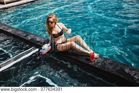 Young Hot Woman Resting At Swimpool. Attractive Girl In Swimsuit Posing On Camera By Sitting At Wate