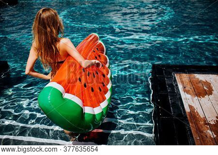 Young Hot Woman Resting At Swimpool. Back View Of Female Model Going Down In Water Steps With Swim R