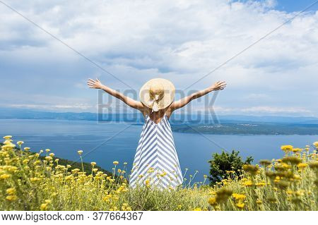 Rear View Of Joung Woman Wearing Striped Summer Dress And Straw Hat Standing In Super Bloom Of Wildf
