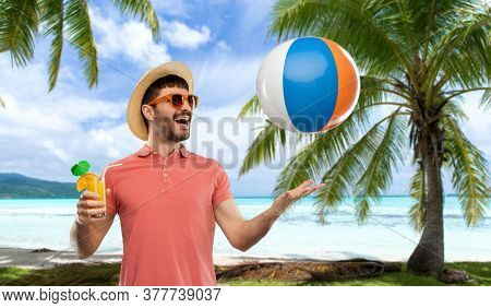 summer, vacation and people concept - happy smiling young man in sunglasses and straw hat with orange juice cocktail and inflatable beach ball over tropical beach background in french polynesia