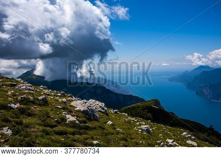 View Of Lake Garda Between Rocks, Clouds And Blue Sky On Monte Altissimo Di Nago In Trento, Italy