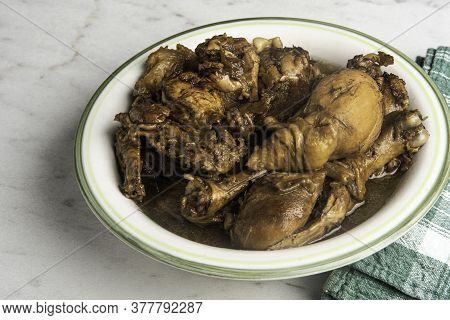 A Serving Of Filipino-style Chicken Adobo Dish In A Bowl With Green Napkin Set On A Marble Tabletop.