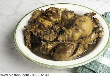A Serving Of Filipino-style Chicken Adobo Dish In A Bowl With Green Napkin Set On A Marble Tabletop.