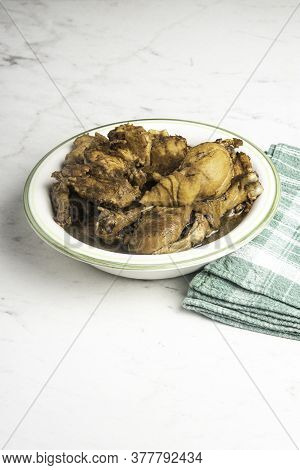 A Serving Of Filipino-style Chicken Adobo Dish In A Bowl With Green Napkin Set On A Marble Tabletop.