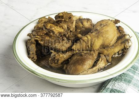 A Serving Of Filipino-style Chicken Adobo Dish In A Bowl With Green Napkin Set On A Marble Tabletop.