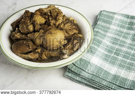 A Serving Of Filipino-style Chicken Adobo Dish In A Bowl With Green Napkin Set On A Marble Tabletop.