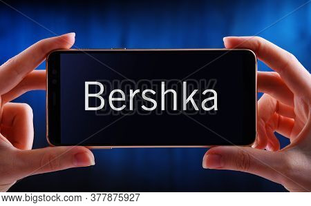Hands Holding Smartphone Displaying Logo Of Bershka