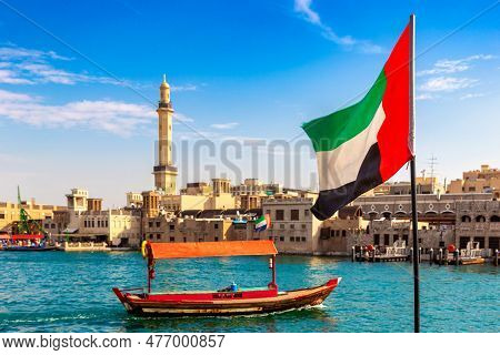 Focus On A Flag Of  United Arab Emirates Flag Against Abra - Old Traditional Wooden Boat And Grand B