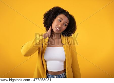Despaired Sad Black Curly Woman Suffering From Neck Pain, Making Massage, Standing On Yellow Backgro