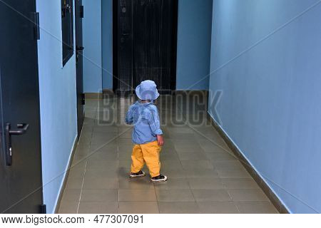 The Toddler Baby Walks In The Entrance Hall On The Floor Near The Apartment Doors. A Child Runs In T